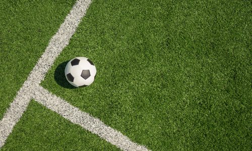 Soccer ball on green grass field with white line corner. Football stadium background. View from above.