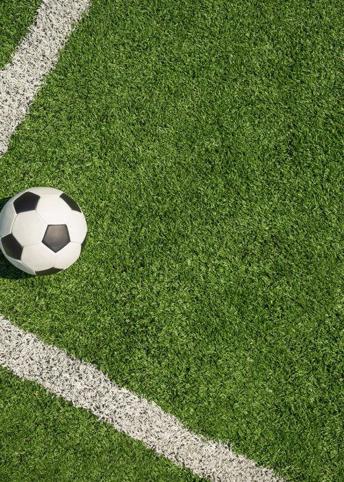 Soccer ball on green grass field with white line corner. Football stadium background. View from above.