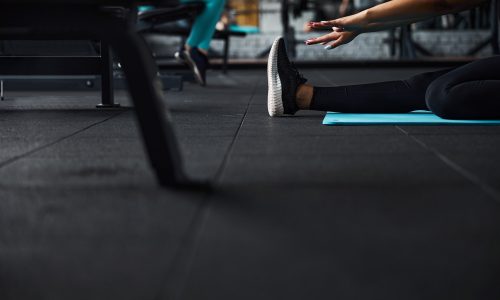 Low angle cropped head close up of female leg in sneaker while she is stretching hands to feet