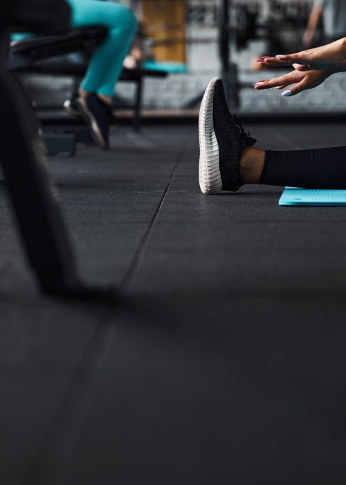 Low angle cropped head close up of female leg in sneaker while she is stretching hands to feet